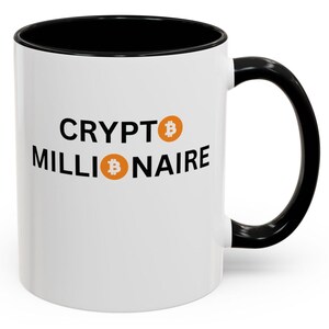 Puede incluir: Taza de cerámica blanca con borde y asa negros. La taza tiene el texto "CRYPTO MILLIONAIRE" en negro con un símbolo de bitcoin a cada lado del texto.