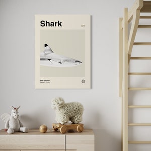 May include: A framed print featuring a grayscale image of a shark, with the word "Shark" in bold black letters at the top. The print is displayed on a light-colored wall above a wooden dresser, with a stuffed unicorn and a sheep toy.