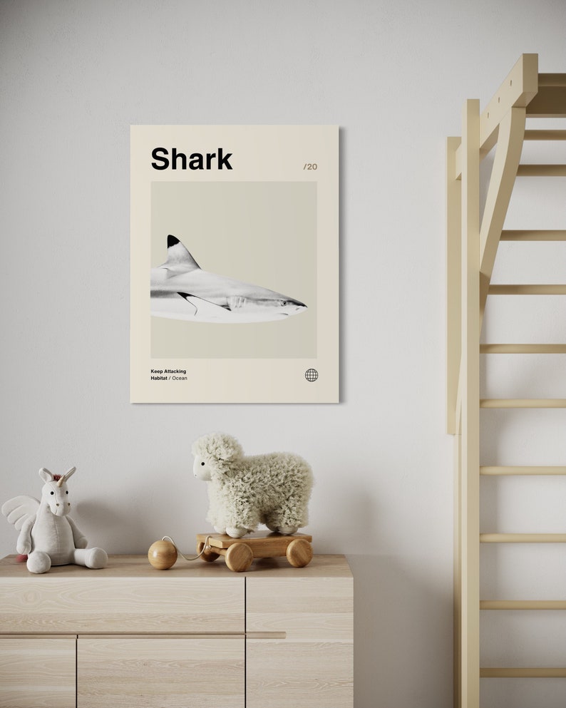 May include: A framed print featuring a grayscale image of a shark, with the word "Shark" in bold black letters at the top. The print is displayed on a light-colored wall above a wooden dresser, with a stuffed unicorn and a sheep toy.
