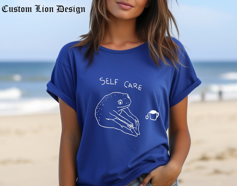 May include: A royal blue t-shirt with a white outline of a frog holding a cup of tea and the text "SELF CARE".