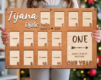 May include: A wooden milestone photo board with the name "Tijana" and the date "April 3 2010". It has slots for photos from newborn to 11 months, plus a "ONE" section. The text "WHOLE YEAR OF AWESOME" and "ONE YEAR" are also visible.