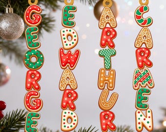 Puede incluir: Adornos navideños de pan de jengibre que deletrean los nombres "GEORGE", "EDWARD", "ARTHUR" y "CARMEN". Cada letra está decorada con glaseado rojo, verde y blanco, y colgada de un hilo dorado. Los adornos se exhiben en un árbol de Navidad.