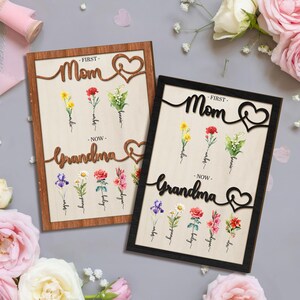 May include: Two framed wood signs with floral illustrations and the text "Mom - First - Grandma - Now" and "Mom - First - Grandma - Now". The signs are in brown and black frames.