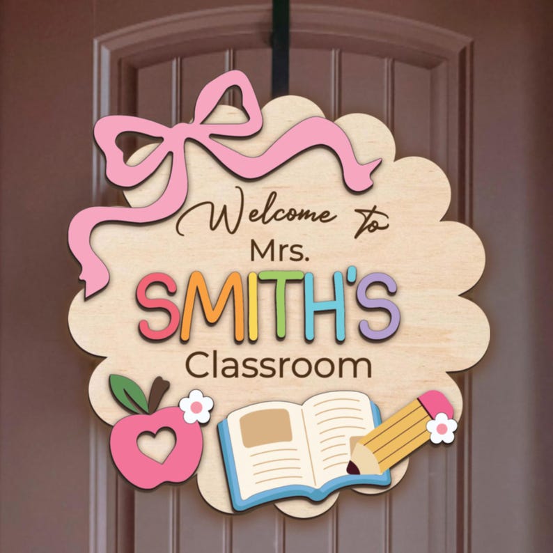 K&ouml;nnte beinhalten: Ein h&ouml;lzernes Willkommensschild f&uuml;r ein Klassenzimmer mit einer rosa Schleife, dem Text "Willkommen in der Klasse von Frau SMITH", einem Apfel, einem Buch und einem Bleistift.