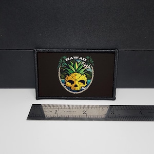 May include: Black rectangular patch featuring a yellow skull-shaped pineapple design with the word "HAWAII" above. The design includes palm trees and ocean imagery. The patch is approximately 3 inches wide.