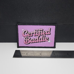 Peut inclure: Écusson rectangulaire avec l'inscription "Certified Baddie" en lettres roses pailletées sur fond violet clair. Le patch est bordé de coutures noires et mesure environ 7,6 cm de long.