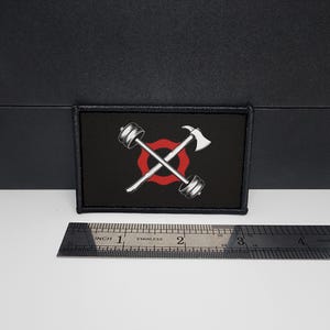 May include: Black rectangular patch with a white barbell and axe crossed over a red circle. The patch is approximately 3 inches long and 2 inches wide. The patch has a black border.