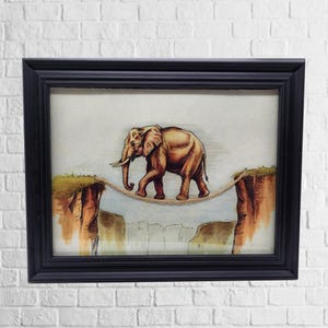 Puede incluir: Obra de arte enmarcada que representa un elefante marrón caminando sobre una cuerda floja tendida entre dos acantilados. La ilustración está sobre un fondo claro, enmarcada en un marco rectangular negro. Los acantilados están pintados en tonos marrones y verdes.