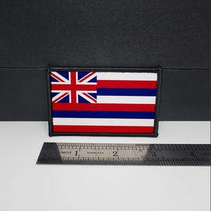 May include: Rectangular patch featuring the flag of Hawaii. The design includes the Union Jack in the upper left corner, with alternating red, white, and blue stripes. The patch is bordered with black stitching and is approximately 7.6 cm wide.