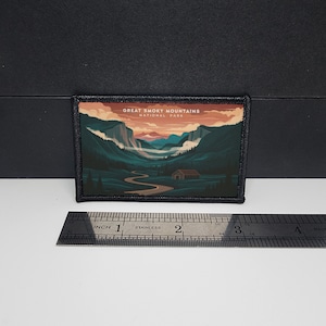 Könnte beinhalten: Rechteckiger Aufnäher mit einer Illustration des Great Smoky Mountains Nationalparks. Das Design zeigt eine kurvenreiche Straße, eine Hütte und Berge unter einem Sonnenuntergang. Der Aufnäher ist ca. 7,6 cm breit und 5,1 cm hoch.