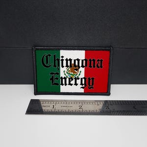 May include: Rectangular patch featuring the Mexican flag design with green, white, and red stripes. The patch has the words "Chingona Energy" in black, stylized lettering. A ruler is placed below the patch for scale.