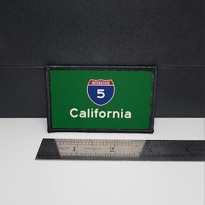 May include: A rectangular patch featuring the Interstate 5 highway sign for California. The patch has a green background with a white and blue highway shield and the word "California" in white. The patch measures approximately 3 inches in length.