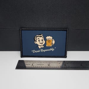 May include: A rectangular patch with a navy blue background features a cartoon man holding a beer mug. The text "Drink Responsibly." is below the image. The patch is approximately 7.6 cm wide.