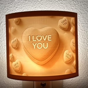 May include: A night light shaped like a heart with the words "I LOVE YOU" on it. The heart is surrounded by smaller hearts with the words "LOVE YOU" on them.