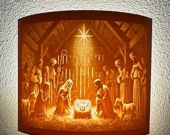 May include: A night light featuring a detailed depiction of the Nativity scene. The warm-toned image shows Mary, Joseph, baby Jesus, and other figures in a stable, illuminated by a star. The night light is plugged into a wall outlet.