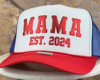 Pode incluir: Um chapéu de caminhoneiro branco e azul com uma parte de trás de malha vermelha. A parte da frente do chapéu tem a palavra "MAMA" em vermelho com o texto "EST. 2024" abaixo.