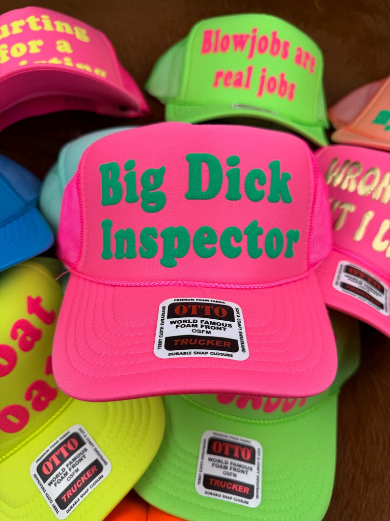 May include: A selection of trucker caps in vibrant neon shades, such as pink, green, and yellow. The caps display striking text in contrasting colours, with phrases like "Big Dick Inspector" and "Blowjobs are real jobs". Each cap has a foam front and a snap closure.