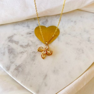 May include: A gold chain necklace with a small, sparkly flower pendant. The pendant is made of gold and has clear stones set in it. The necklace is on a white marble surface.