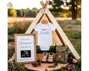 Può includere: Annuncio di nascita con un body bianco con la scritta "Baby Jacobs". Un cartello incorniciato recita "Our Little Camper is on the Way. Arriving Dec 2025". Include stivali da bambino, una borsa verde e un piccolo teepee.