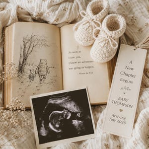 Può includere: Un libro aperto con un'illustrazione di Winnie the Pooh, una foto di ecografia e un segnalibro con la scritta "A New Chapter Begins". Sono presenti anche due piccoli stivaletti per neonati in maglia color crema. Il segnalibro indica un arrivo a luglio 2026.