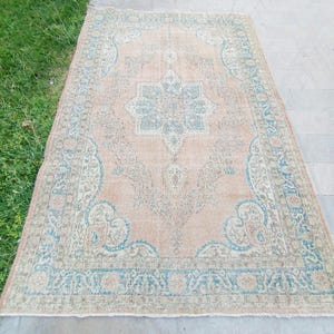 May include: A rectangular, vintage-style rug with a peach-colored central field and a detailed border. The rug features a central medallion and ornate patterns in shades of blue and cream, creating a classic, aged aesthetic.