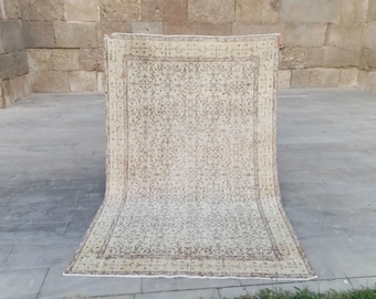 May include: A beige and brown patterned rug with a rectangular shape. The rug features an intricate floral design and a dark brown border. The rug is displayed outdoors, partially rolled out on a concrete surface.