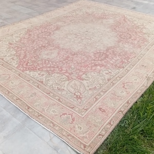 May include: A rectangular area rug featuring a faded pink and cream colour palette with an intricate floral medallion pattern in the centre and a detailed border. The rug has a distressed appearance with visible woven textures throughout the surface.