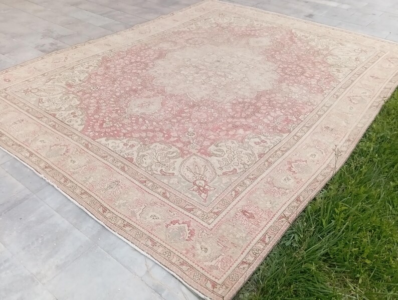 May include: A rectangular area rug featuring a faded pink and cream colour palette with an intricate floral medallion pattern in the centre and a detailed border. The rug has a distressed appearance with visible woven textures throughout the surface.