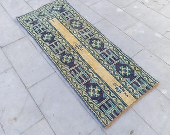 Puede incluir: Una alfombra larga y estrecha con un patrón geométrico en tonos de azul, verde y amarillo. La alfombra tiene una franja central amarilla y está bordeada por un patrón repetido de azul y verde.