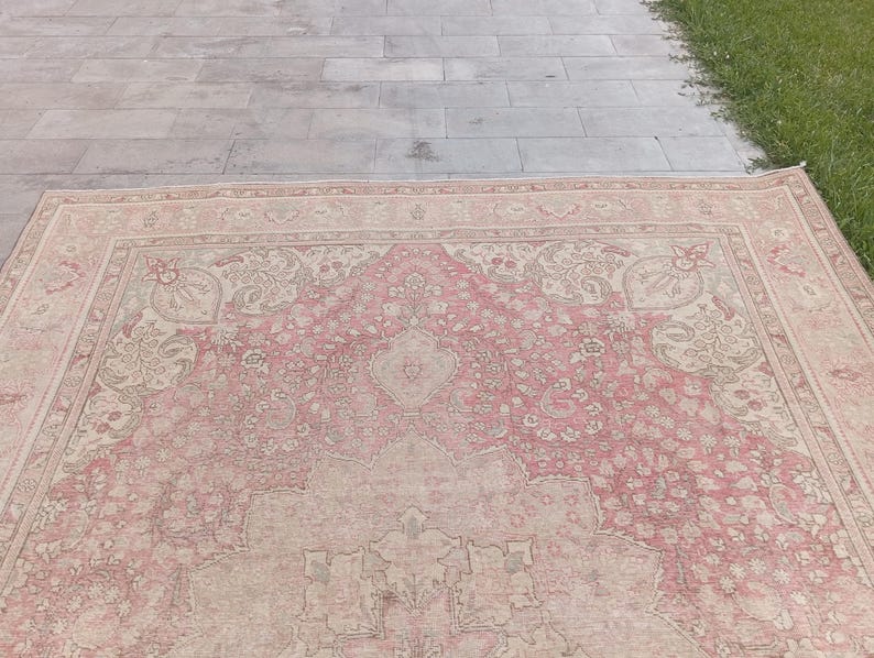 May include: A large rectangular area rug featuring a faded pink and beige colour palette. The rug displays an intricate, symmetrical floral pattern with a central medallion and detailed border motifs woven throughout the entire surface area.