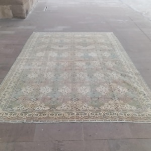 May include: A rectangular, faded-look rug with a detailed floral pattern in shades of beige, green, and blue. The rug has a decorative border and is placed on a stone surface.