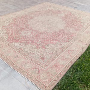 May include: A large rectangular area rug featuring a central medallion design with intricate floral and vine patterns. The colour palette consists of soft dusty pink and muted beige tones, framed by a wide decorative border with repeating motifs.