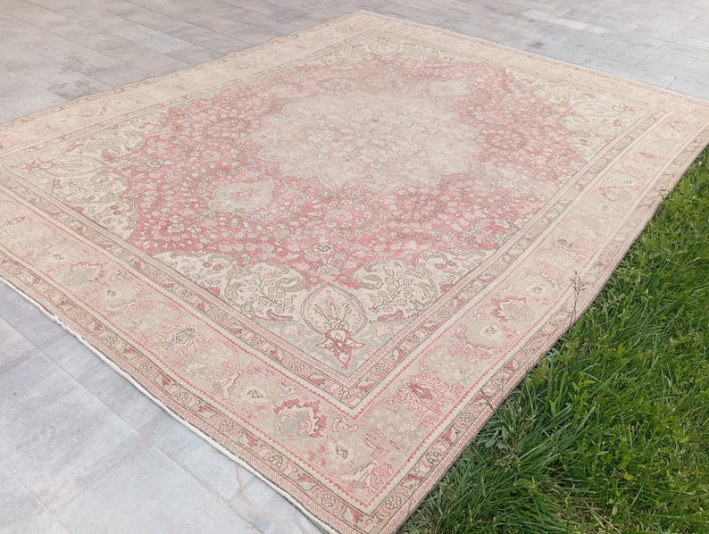 May include: A large rectangular area rug featuring a central medallion design with intricate floral and vine patterns. The colour palette consists of soft dusty pink and muted beige tones, framed by a wide decorative border with repeating motifs.