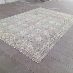 May include: A rectangular, vintage-style rug with a faded, distressed appearance. The rug features a central pattern in shades of pale green, pink, and blue, surrounded by a detailed border in cream and beige tones. The rug is placed on a wooden floor.