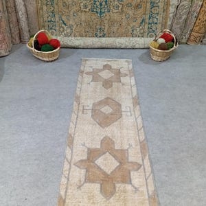 May include: A long, rectangular beige rug with a brown geometric pattern. The rug has a faded, vintage look.