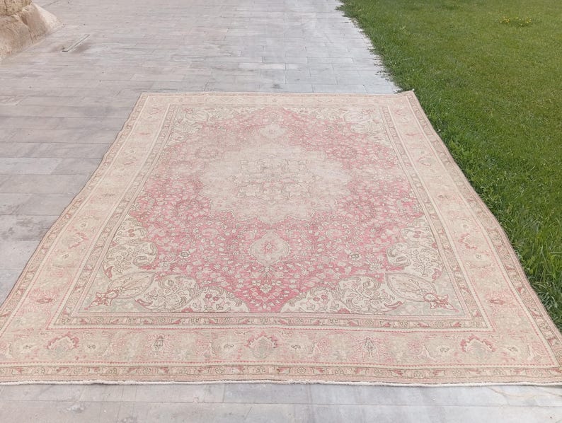 May include: A rectangular area rug featuring a central medallion design with intricate floral and vine patterns. The colour palette consists of soft dusty pink and cream tones, with a wide decorative border framing the detailed interior motif.
