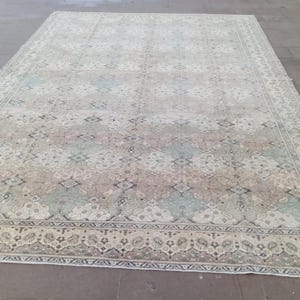 May include: Large rectangular area rug with a faded, vintage appearance. The rug features a central pattern of muted blues, pinks, and tans, framed by a detailed border. The overall design suggests a traditional, oriental style.
