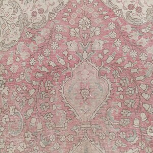 May include: A woven rug featuring a central medallion design in shades of dusty rose, cream, and muted sage green. The surface displays intricate floral motifs, scrolling vines, and geometric patterns throughout the field, framed by a linear border.