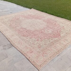 May include: A large rectangular area rug featuring a faded pink and cream colour palette. The rug displays an intricate, symmetrical floral pattern with a central medallion and a detailed border, showcasing a worn, weathered texture throughout.