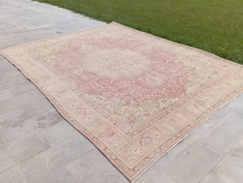 May include: A large rectangular area rug featuring a faded pink and cream colour palette. The rug displays an intricate, symmetrical floral pattern with a central medallion and a detailed border, showcasing a worn, weathered texture throughout.