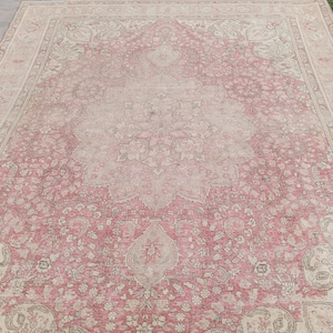 May include: A large rectangular area rug featuring a central floral medallion pattern in shades of dusty pink and cream. The rug displays intricate botanical motifs, scrolling vines, and a wide decorative border with repeating floral elements.
