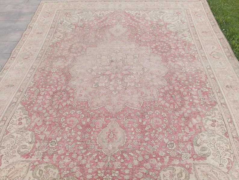May include: A large rectangular area rug featuring a central floral medallion pattern in shades of dusty pink and cream. The rug displays intricate botanical motifs, scrolling vines, and a wide decorative border with repeating floral elements.
