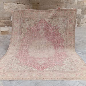May include: A large rectangular area rug featuring a central medallion design in shades of dusty rose and cream. The rug is decorated with intricate floral and vine patterns throughout the field and a wide, detailed border in matching tones.