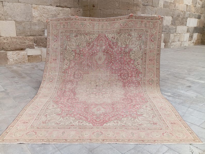 May include: A large rectangular area rug featuring a central medallion design in shades of dusty rose and cream. The rug is decorated with intricate floral and vine patterns throughout the field and a wide, detailed border in matching tones.