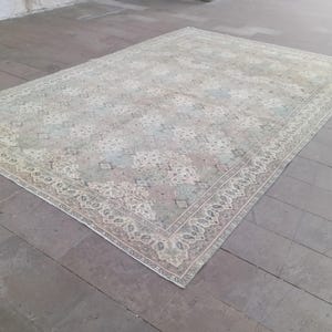 May include: A rectangular, vintage-style rug with an intricate floral pattern in muted tones of beige, pink, and blue. The rug has a detailed border and is placed on a gray tiled floor. The overall aesthetic is antique and elegant.