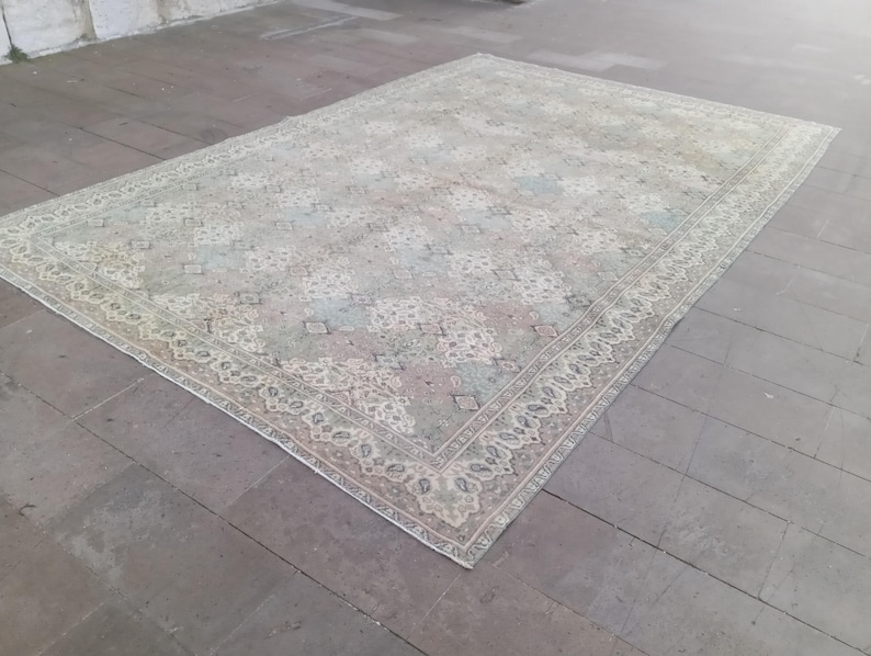 May include: A rectangular, vintage-style rug with an intricate floral pattern in muted tones of beige, pink, and blue. The rug has a detailed border and is placed on a gray tiled floor. The overall aesthetic is antique and elegant.