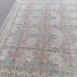 May include: An antique area rug with a faded, distressed appearance. The rug features a repeating pattern of floral and geometric motifs in muted tones of beige, blue, and rose. A detailed border frames the central design.