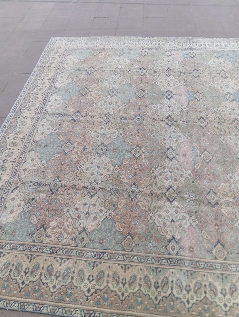 May include: An antique area rug with a faded, distressed appearance. The rug features a repeating pattern of floral and geometric motifs in muted tones of beige, blue, and rose. A detailed border frames the central design.