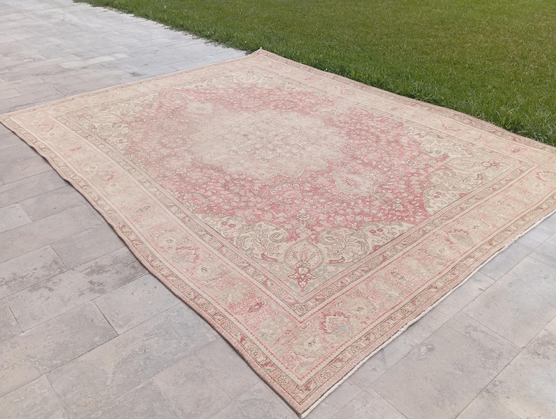May include: A large rectangular area rug featuring a faded pink and cream colour palette with an intricate floral medallion pattern in the centre and a detailed border design. The rug has a low pile texture and a symmetrical, ornate woven motif.