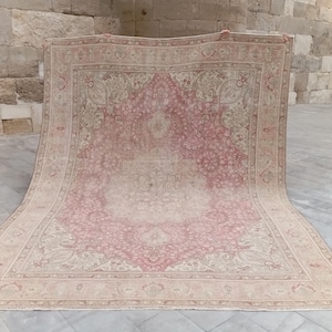 May include: A large rectangular area rug featuring a central medallion design in shades of dusty rose and cream. The rug displays an intricate floral pattern throughout the field and a wide decorative border with repeating motifs in muted tones.